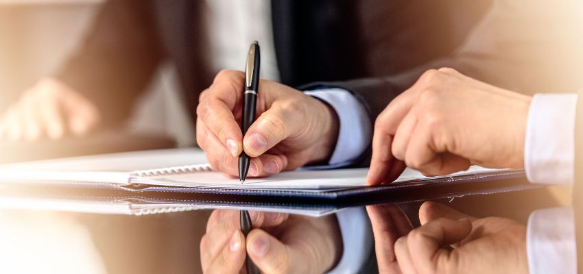 A professional signs a document on a hard copy.