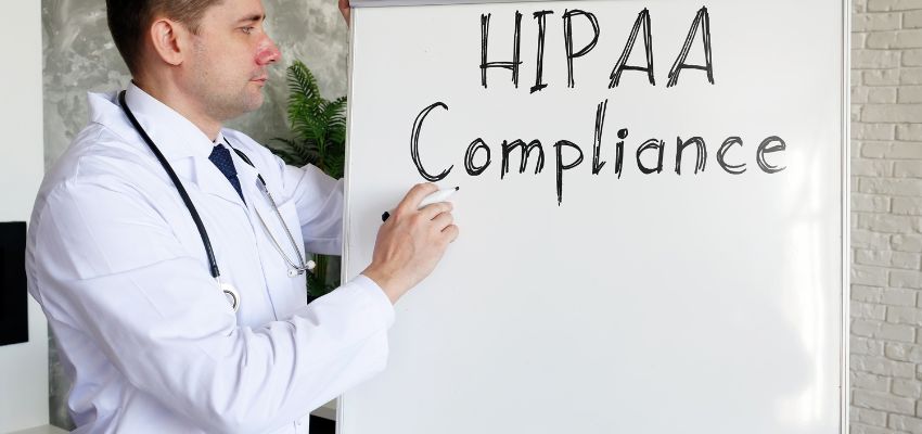 A doctor writes HIPAA Compliance on the whiteboard.