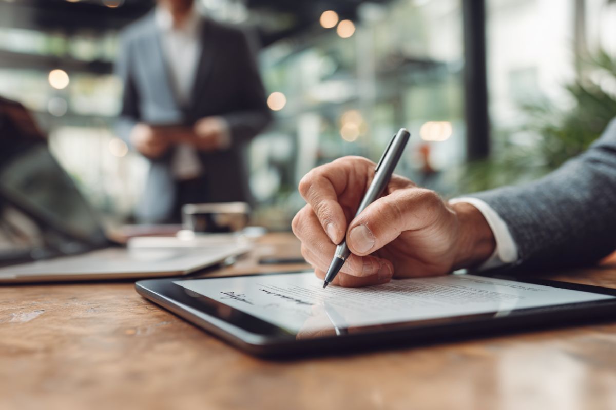 Primer plano de un hombre firmando un documento digital en una tableta como firmante autorizado.