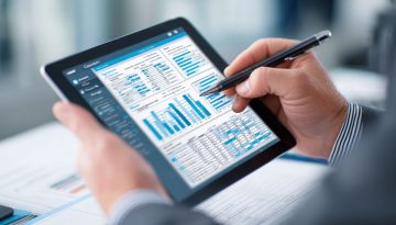 Ein Geschäftsmann benutzt einen Stift, um detaillierte Finanzberichte und Balkendiagramme auf einem Tablet zu kommentieren, und führt eine gründliche Vertragsprüfung auf Einhaltung und Genauigkeit durch.