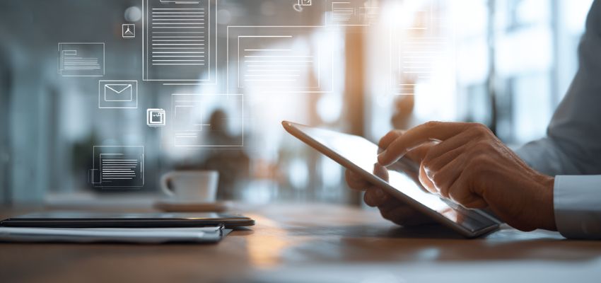 Profesional de los negocios en una oficina moderna interactuando con una tableta que muestra documentos digitales, correos electrónicos e iconos, impulsada por un avanzado software de colaboración contractual para flujos de trabajo en equipo sin interrupciones.