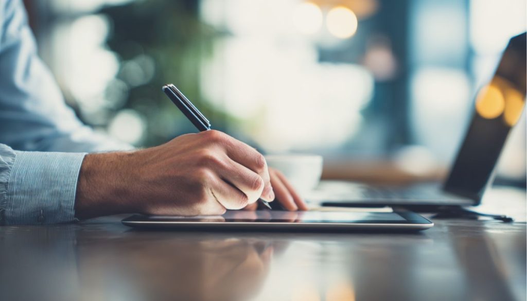 A business professional signs a contract addendum on a digital tablet using a stylus at a modern workspace